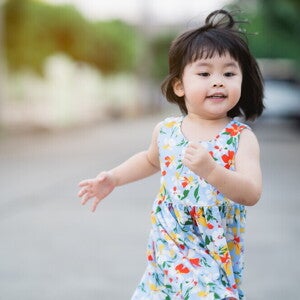 Asian female toddler runs in the street during summertime.