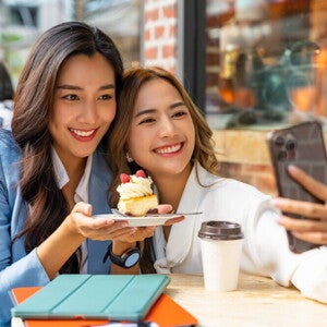 Teaser_Image Two Asian working moms take a selfie after meeting for dessert during lunch break.