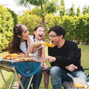 8 Simple Ways to Inspire Healthy Eating Habits in the Whole Family Asian family enjoying barbecued corn outdoors.