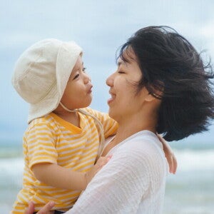 Asian young mom smiles at her talkative toddler son in her arms during a day out in the beach. 