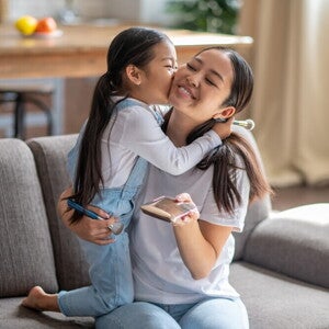Know Your Solo Parent Benefits in the Philippines Preschool-age child kisses her mom, a solo parent, while they’re in the living room.