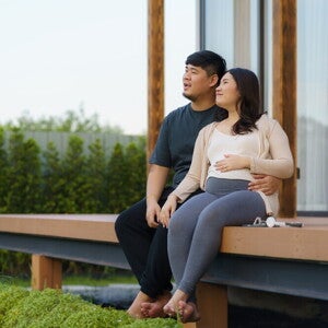 Asian pregnant couple sit on the porch of their vacation home during their babymoon