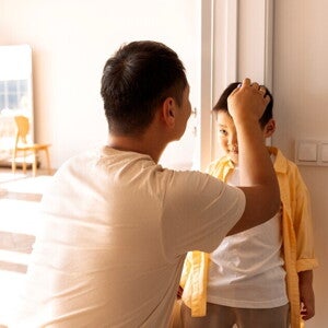 Asian dad marks his son's height on the wall to record growth milestone. Asian dad marks his son's height on the wall to record growth milestone.