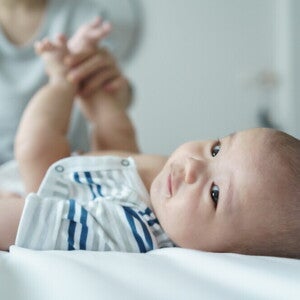 A young Asian mother changing her baby's diaper on a bed.