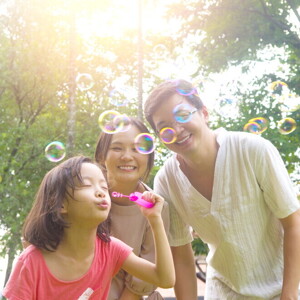 Filipino parents watch their daughter blow bubbles during a hot day.