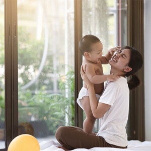 Smiling Asian mom holding her clapping baby while seated on cushions on the floor Smiling Asian mom holding her clapping baby while seated on cushions on the floor