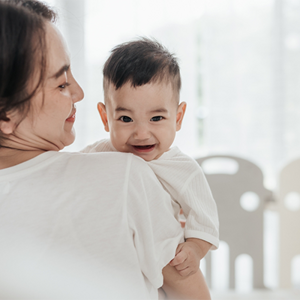 Smiling Asian mom with her laughing baby enjoys the early childhood stage