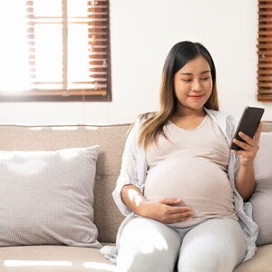 Smiling Asian pregnant woman who is 38 weeks pregnant checks her phone Smiling Asian pregnant woman who is 38 weeks pregnant checks her phone