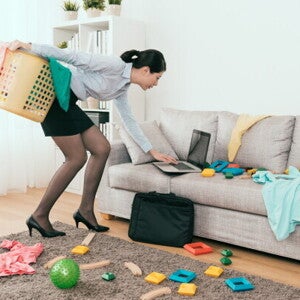 Young Asian mom stressed at messy living room with toys and laundry, trying to tidy up.