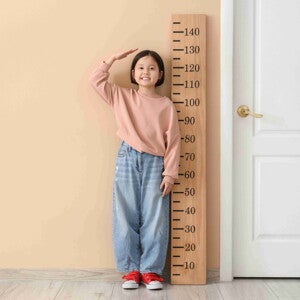 Asian female child stands beside a life-size ruler to measure height for BMI checkup. Asian female child stands beside a life-size ruler to measure height for BMI checkup.