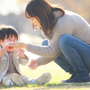 Asian mom comforts her little boy to help his emotional regulation as he cries outdoors.