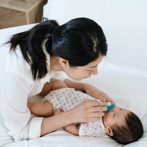 Asian mom giving pacifier to little Asian newborn.