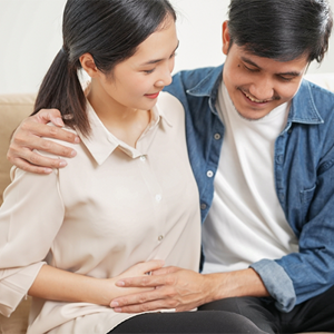 Young Asian 6 weeks pregnant woman with her husband holding her belly on the sofa