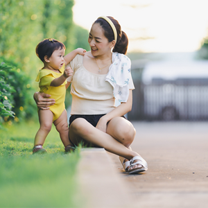 Young Asian mom supports her baby who's practicing their motor skills while outdoors.