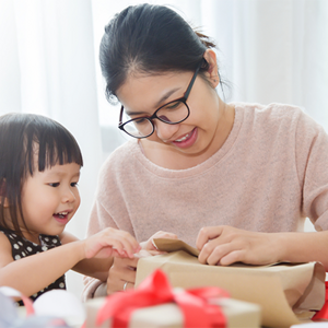 Young Asian mom wraps Christmas gifts and gets some help from her toddler daughter.