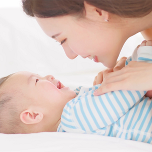 Young Asian mother plays with her happy baby on the bed.