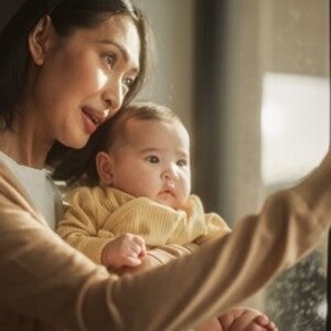 Young Asian woman and baby looking at the rain outside their window