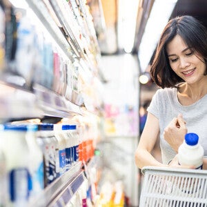 Young Asian woman putting a milk bottle in her basket after choosing from the types of milk in the supermarket