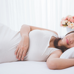 Young pregnant Asian woman lies on her left side in bed, one of the ideal pregnancy sleeping positions