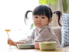 Asian female toddler prepares to eat as she holds her fork with food