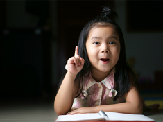 Asian preschool-age girl raises her index finger to gesture number 1.