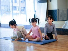 Three Adorable Asian preschoolers with healthy tummies sit on a yoga mat in fitness studio