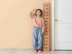 Asian female child stands beside a life-size ruler to measure height for BMI checkup.