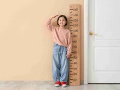 Asian girl checking her height against wall ruler.