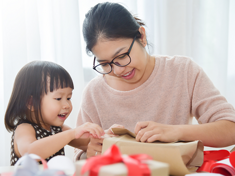 Young Asian mom wraps Christmas gifts and gets some help from her toddler daughter.