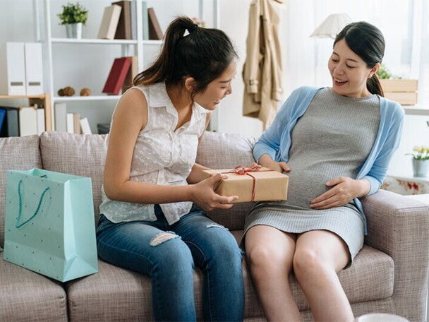 A young Asian pregnant woman receiving a gift from her friend during her baby shower at home.