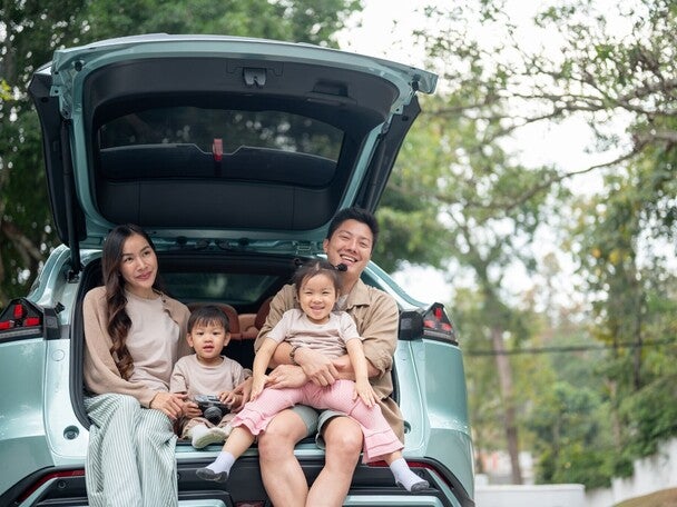 A happy Asian family sitting in the trunk of their car, enjoying a pit stop on their road trip.