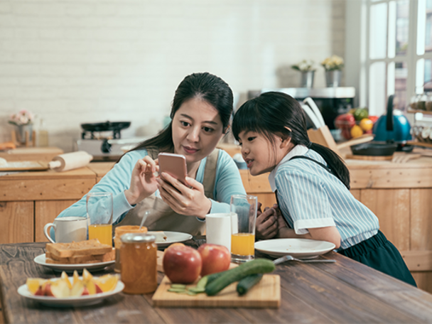 Asian mother with her daughter checking her smartphone at the kitchen table