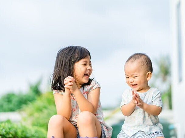 Asian preschool-age girl and her baby brother laugh as they play a game outdoors