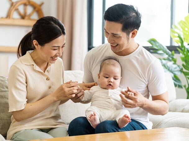 Filipino mom smiles at her newborn who's being held by her husband on his lap.