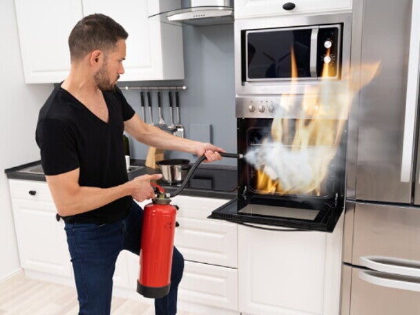 A young man using a fire extinguisher to put out a fire in an oven after learning fire safety tips. 