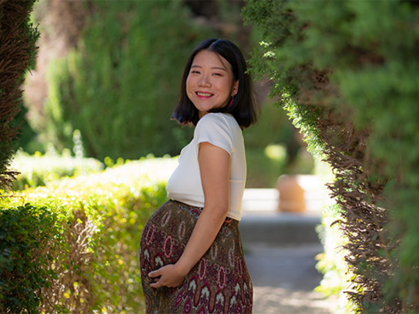 Smiling pregnant Asian woman wearing a cotton dress outdoors and showing off her baby bump.