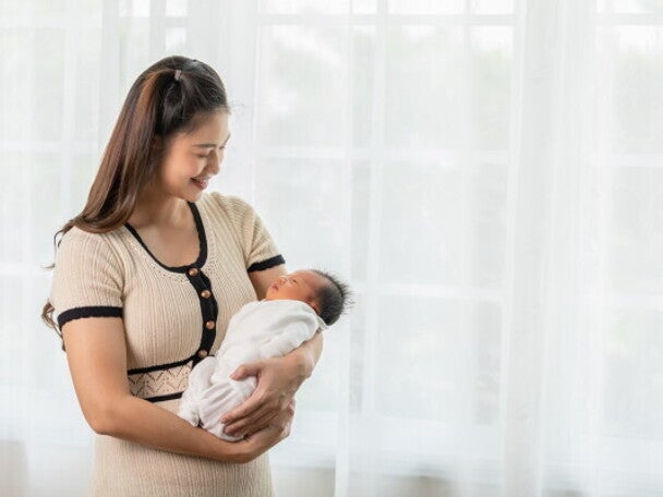 A new mom holding her newborn baby while standing at home, happy with her self-care plan.