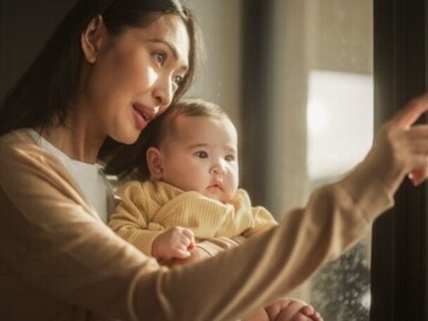Young Asian woman and baby looking at the rain outside their window