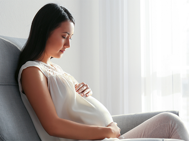 A young woman holding her belly while seated at 16 weeks pregnant. A young woman holding her belly while seated at 16 weeks pregnant.
