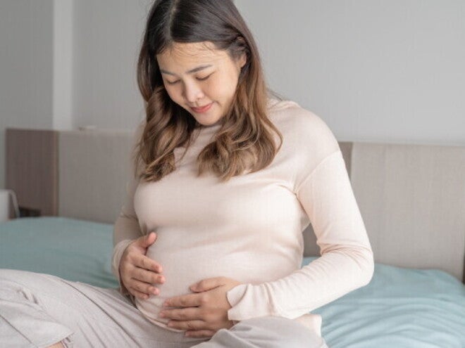 Pregnant Asian young woman who is 32 weeks pregnant stares at her baby bump 