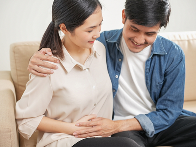 Young Asian 6 weeks pregnant woman with her husband holding her belly on the sofa