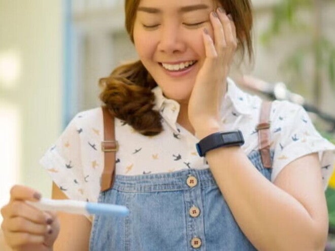Asian woman in denim jumping smiling at pregnancy test results. Asian woman in denim jumping smiling at pregnancy test results.