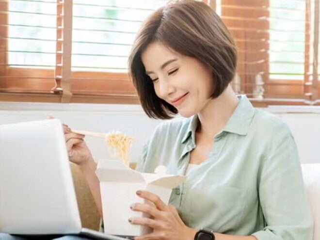 Young Filipina experiences a food craving and enjoys takeout while sitting on the sofa with her laptop on her lap. Young Filipina experiences a food craving and enjoys takeout while sitting on the sofa with her laptop on her lap.