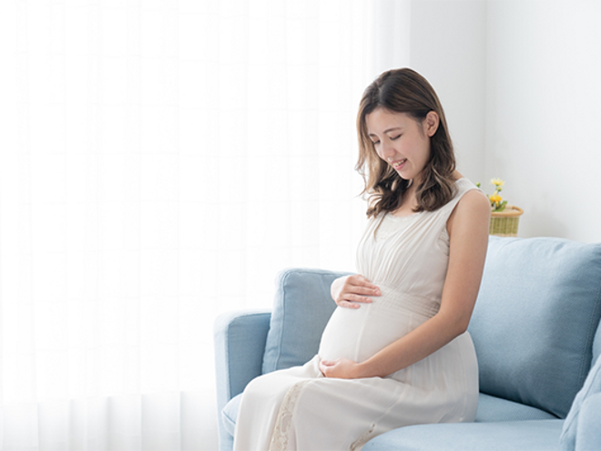 A 29 weeks pregnant Asian woman lovingly holding and looking at her belly at home