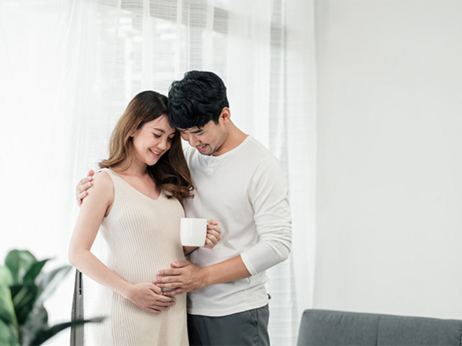 A 7 weeks pregnant Asian woman standing while her husband holds her close with a hand on her belly. A 7 weeks pregnant Asian woman standing while her husband holds her close with a hand on her belly.