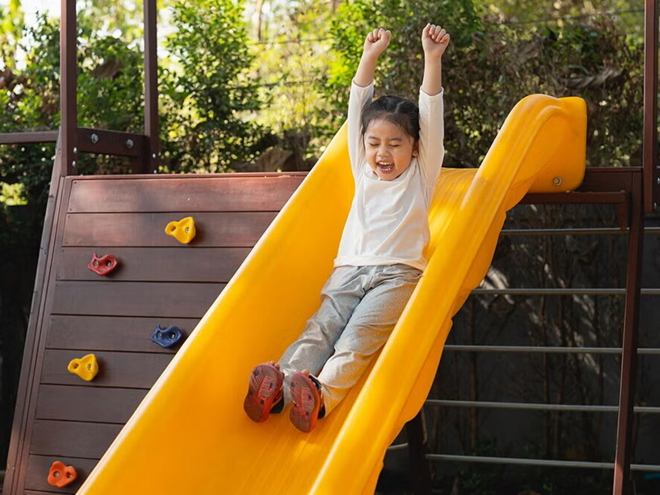 A happy child sliding down a playground slide outdoors, representing active play, childhood joy,  and the importance of supporting kids’ immune and respiratory health