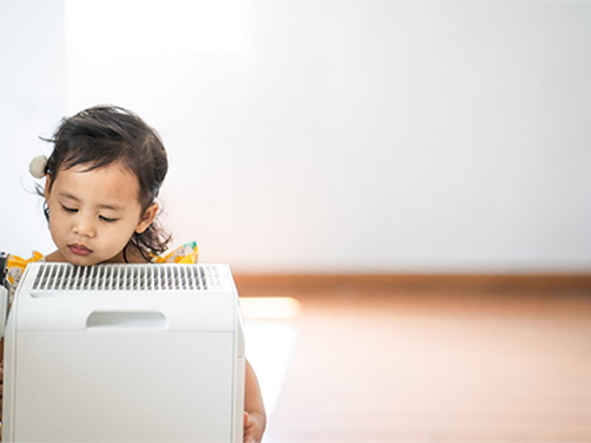 A photo of a little girl breathing in clean air from an air purifier at home