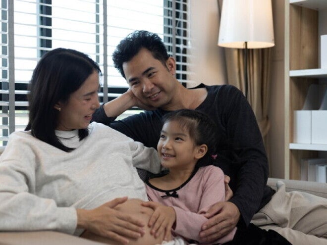 A pregnant woman and her husband with their stepdaughter on a couch, happy as a blended family.