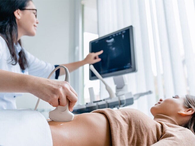A smiling Asian pregnant woman undergoes an ultrasound scan with her ob-gyn for pregnancy complications A smiling Asian pregnant woman undergoes an ultrasound scan with her ob-gyn for pregnancy complications