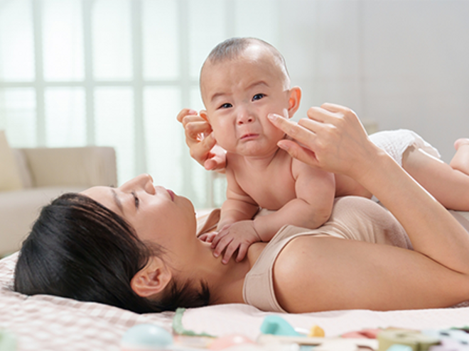 A young Asian mom lying in bed keeping her tearful baby close to her, knowing why babies cry